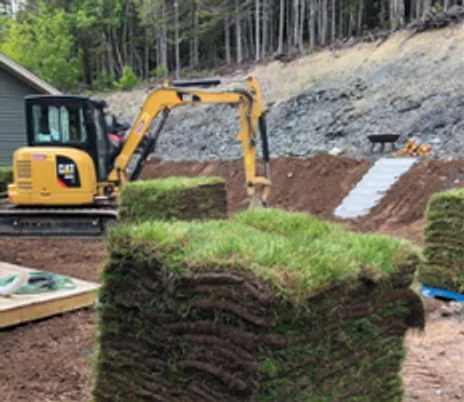 Yellow excavator and a pallet of sod on a graded slope