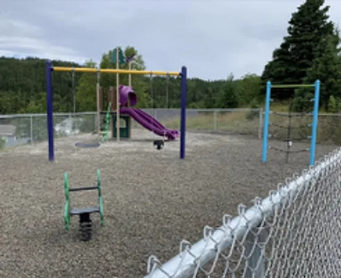 Chain-link fence beside a playground with a purple slide and swing frames